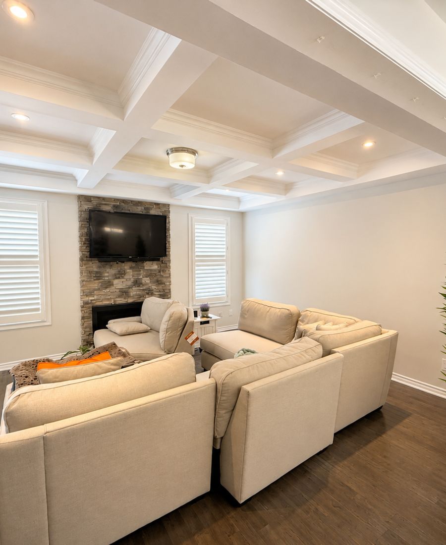 Bright common living area with coffered ceiling, beige sectional sofa, stone accent wall, plantation shutters, and hardwood floors in Merivale