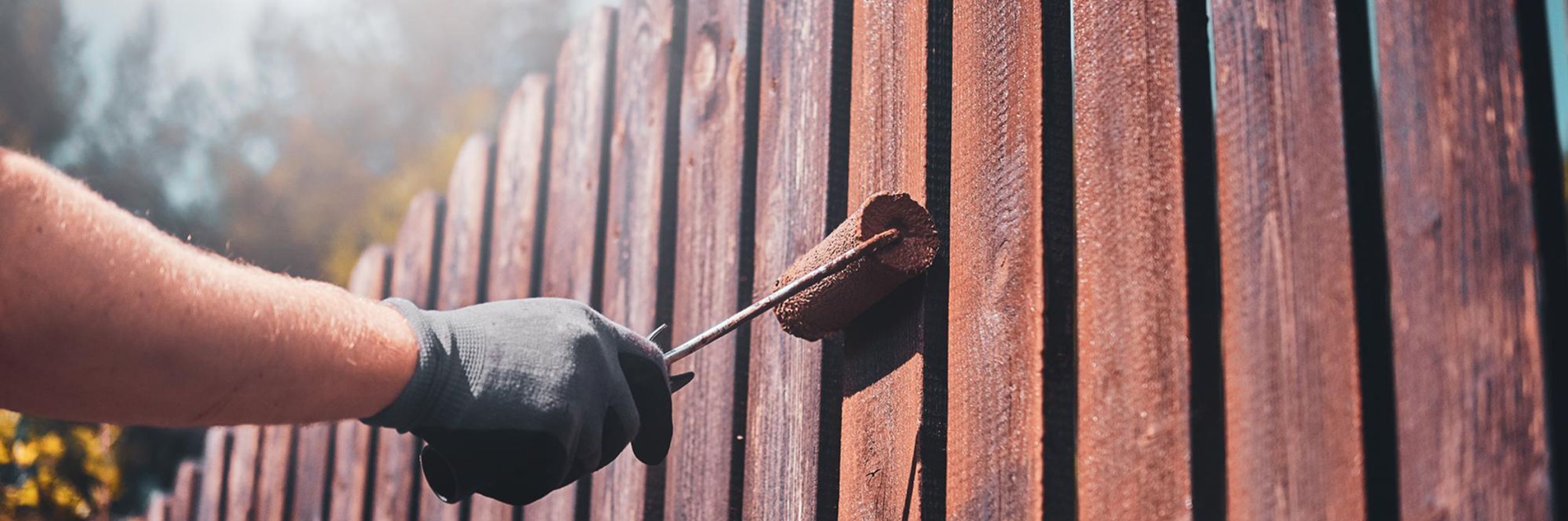 Person rolling stain on fence