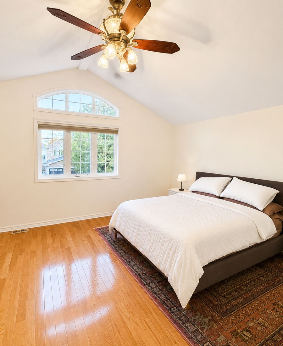 Bright master bedroom with vaulted ceilings, warm neutral walls, polished hardwood floors, and a large arched window in Stittsville
