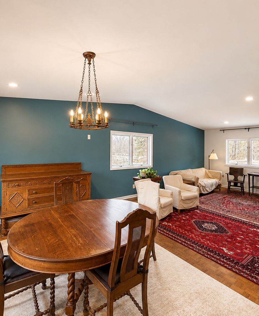 Dining and living space with deep teal accent wall, warm wooden dining table, antique chandelier, and Persian rugs over hardwood floors in Oxford Mills
